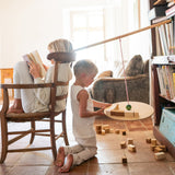 A child playing with the Grapat wooden pendulum set with wooden blocks on the floor