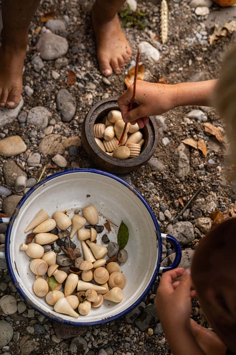 Close up of children playing with the Grapat eco-friendly natural wood mandala pieces in a white bowl on some small pebbles