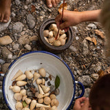 Close up of children playing with the Grapat eco-friendly natural wood mandala pieces in a white bowl on some small pebbles