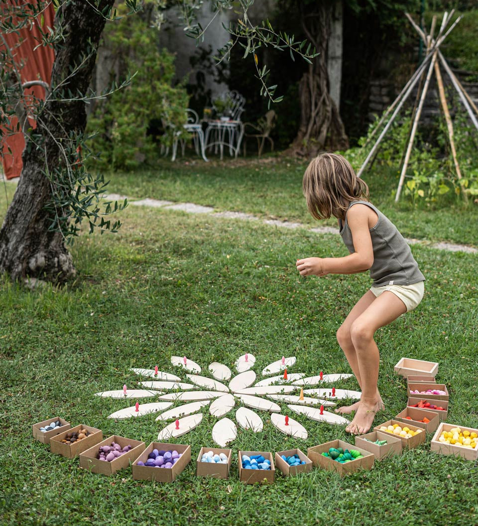 Young girl playing with grapat mandala pieces and the wooden petal platforms on some grass