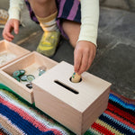 Close up of child's hand putting a Grapat nin inside the Grapat wooden permanence box on a striped blanket