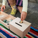 Close up of child's hand putting a Grapat nin inside the Grapat wooden permanence box on a striped blanket