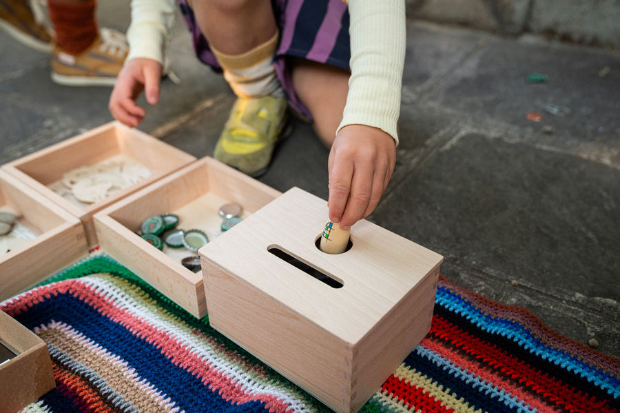 Close up of child's hand putting a Grapat nin inside the Grapat wooden permanence box on a striped blanket