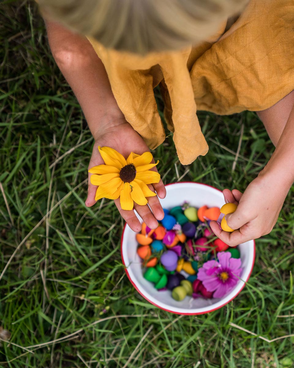 Close up of girl holding a yellow flower and some Grapat wooden mandala mushrooms over a bowl of mandala pieces