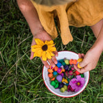 Close up of girl holding a yellow flower and some Grapat wooden mandala mushrooms over a bowl of mandala pieces