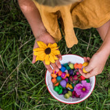 Close up of girl holding a yellow flower and some Grapat wooden mandala mushrooms over a bowl of mandala pieces