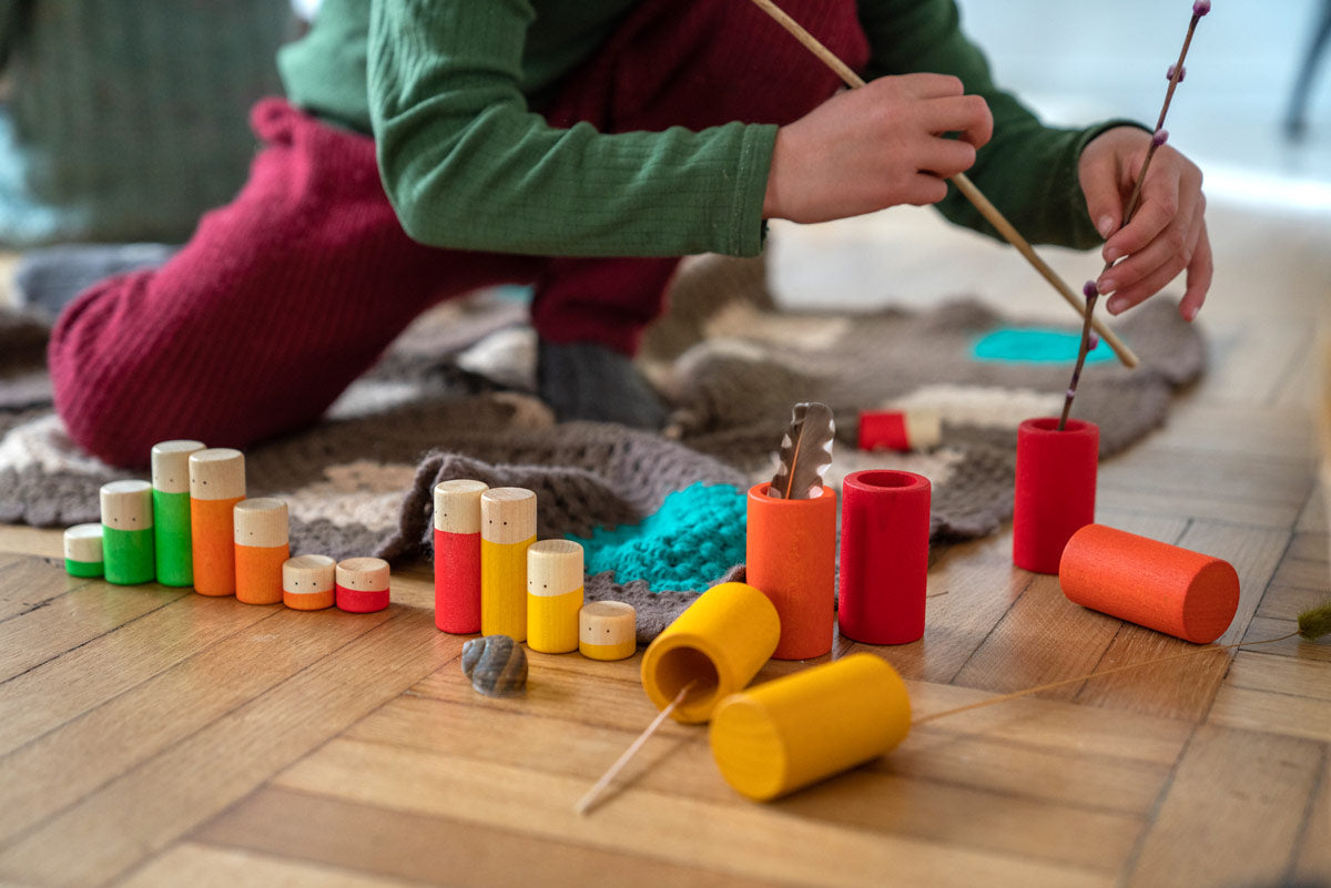 Close up of child playing with some sticks and the Grapat Waldorf wooden Lo toy figures