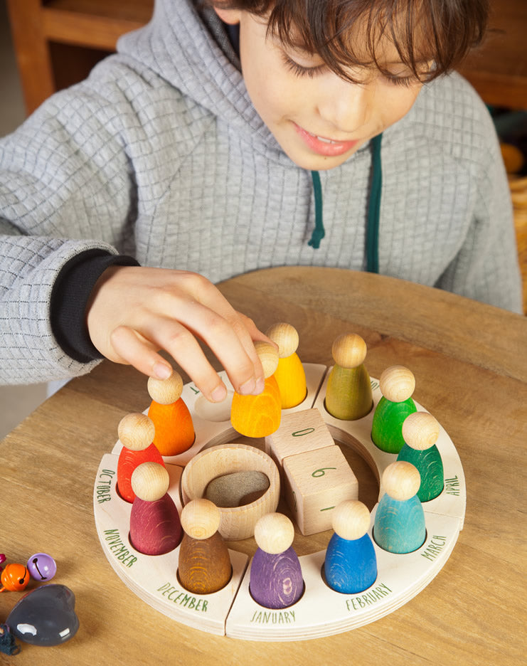 Grapat English Perpetual Calendar displaying the 12 nin peg dolls in colours representing the months of the year according to Waldorf teachings. The display ring has each month written in English around the edge and two cubes in the centre to mark the day