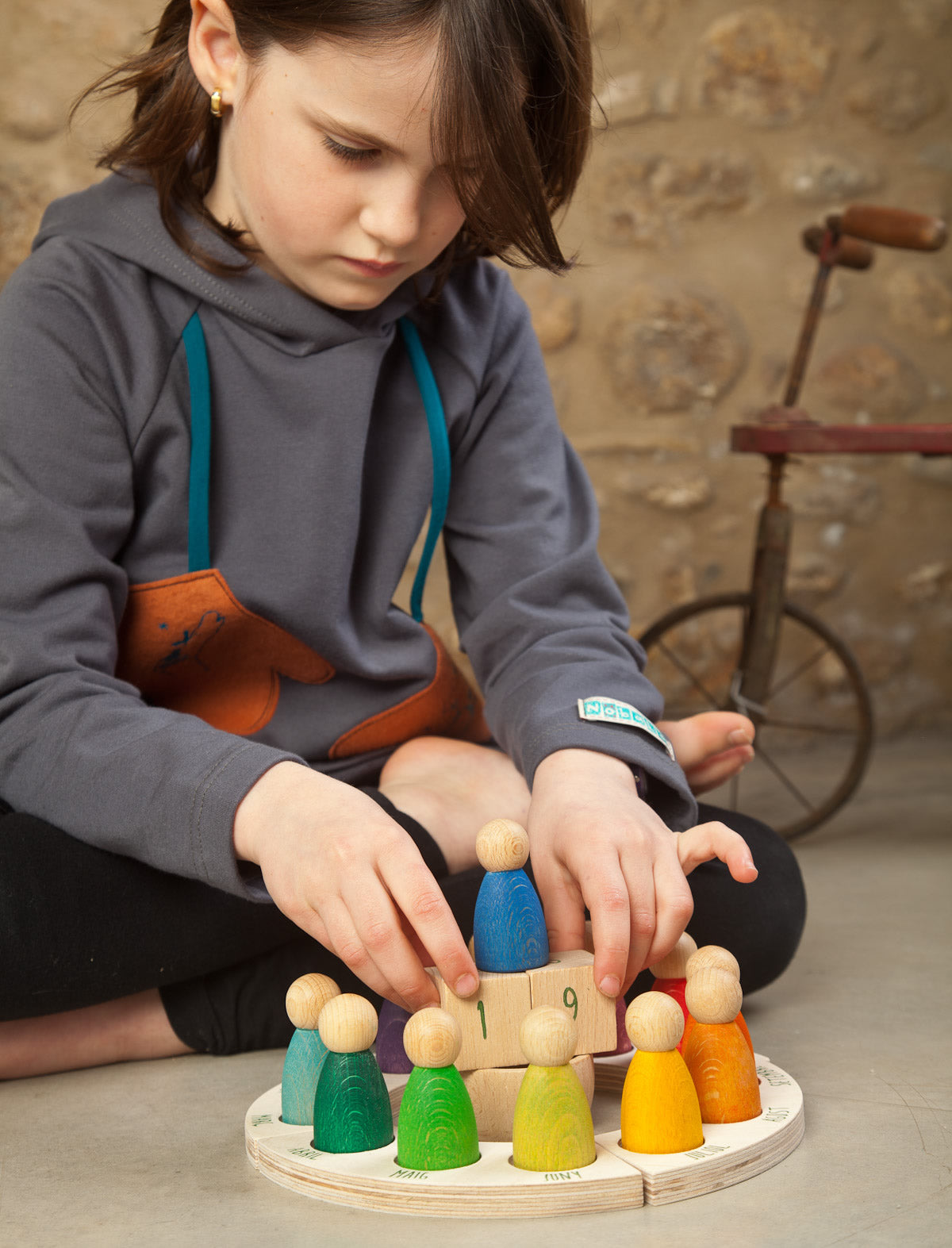 Grapat English Perpetual Calendar displaying the 12 nin peg dolls in colours representing the months of the year according to Waldorf teachings. The display ring has each month written in English around the edge and two cubes in the centre to mark the day