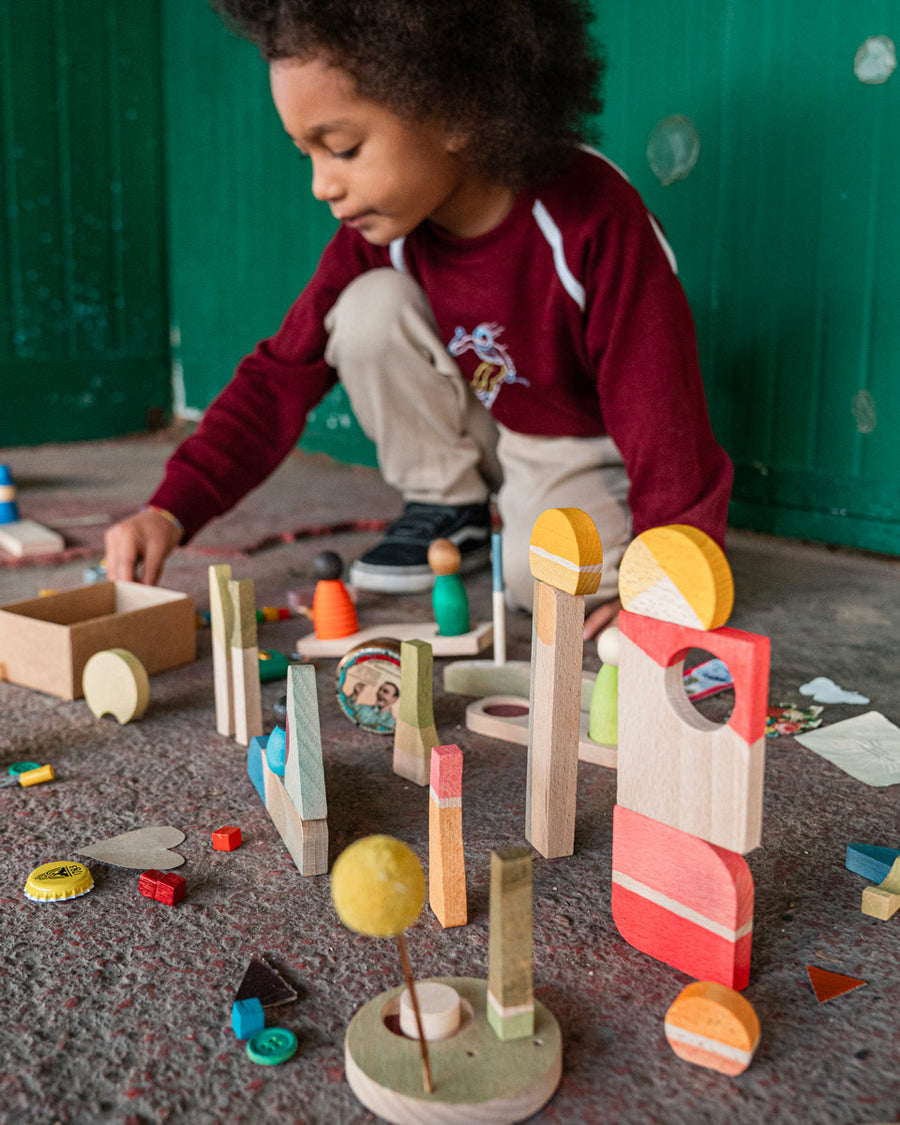 Child crouched down on the floor building towers with the Grapat happy place Waldorf toy set