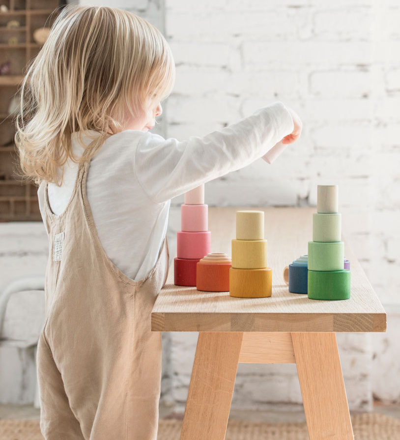 A child playing with the Grapat Nesting Bowls on a wooden table. 