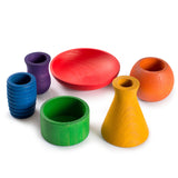 A child playfully pouring sand from their hand to fill up the blue pot of the Grapat Wooden Rainbow Sorting Pots