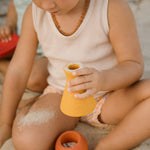 A child playfully pouring sand from the red bowl and purple vase of the Grapat Wooden Rainbow Sorting Pots