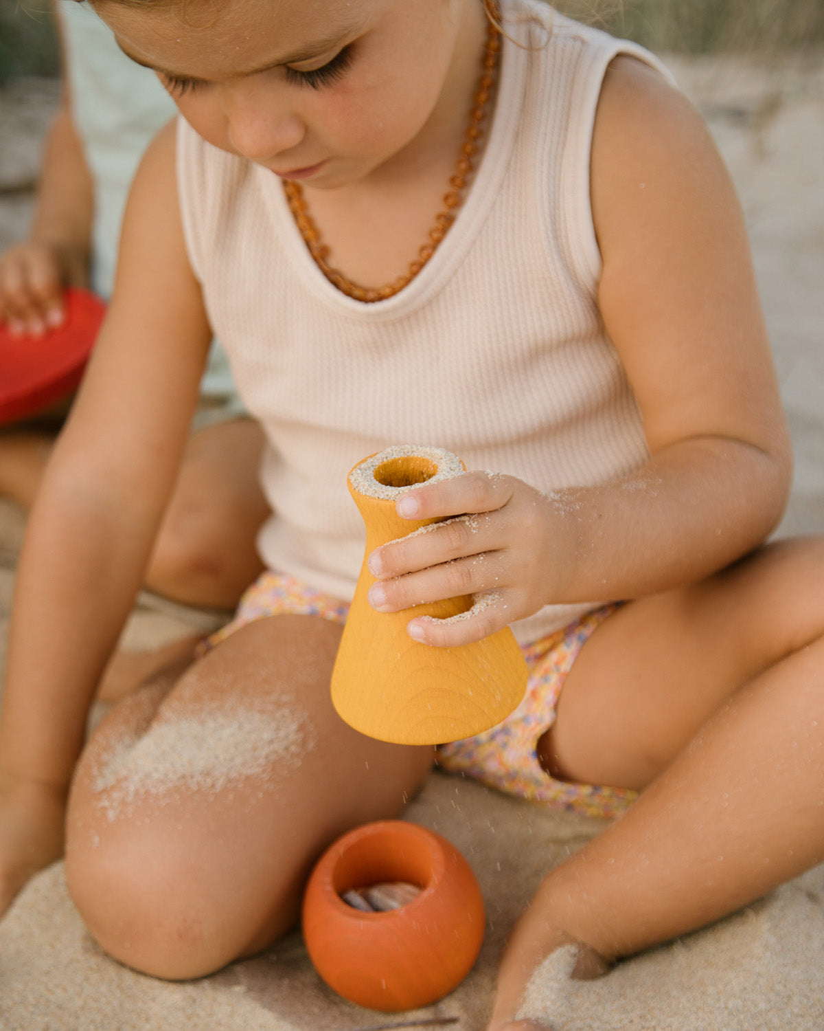 A child playfully pouring sand from the red bowl and purple vase of the Grapat Wooden Rainbow Sorting Pots