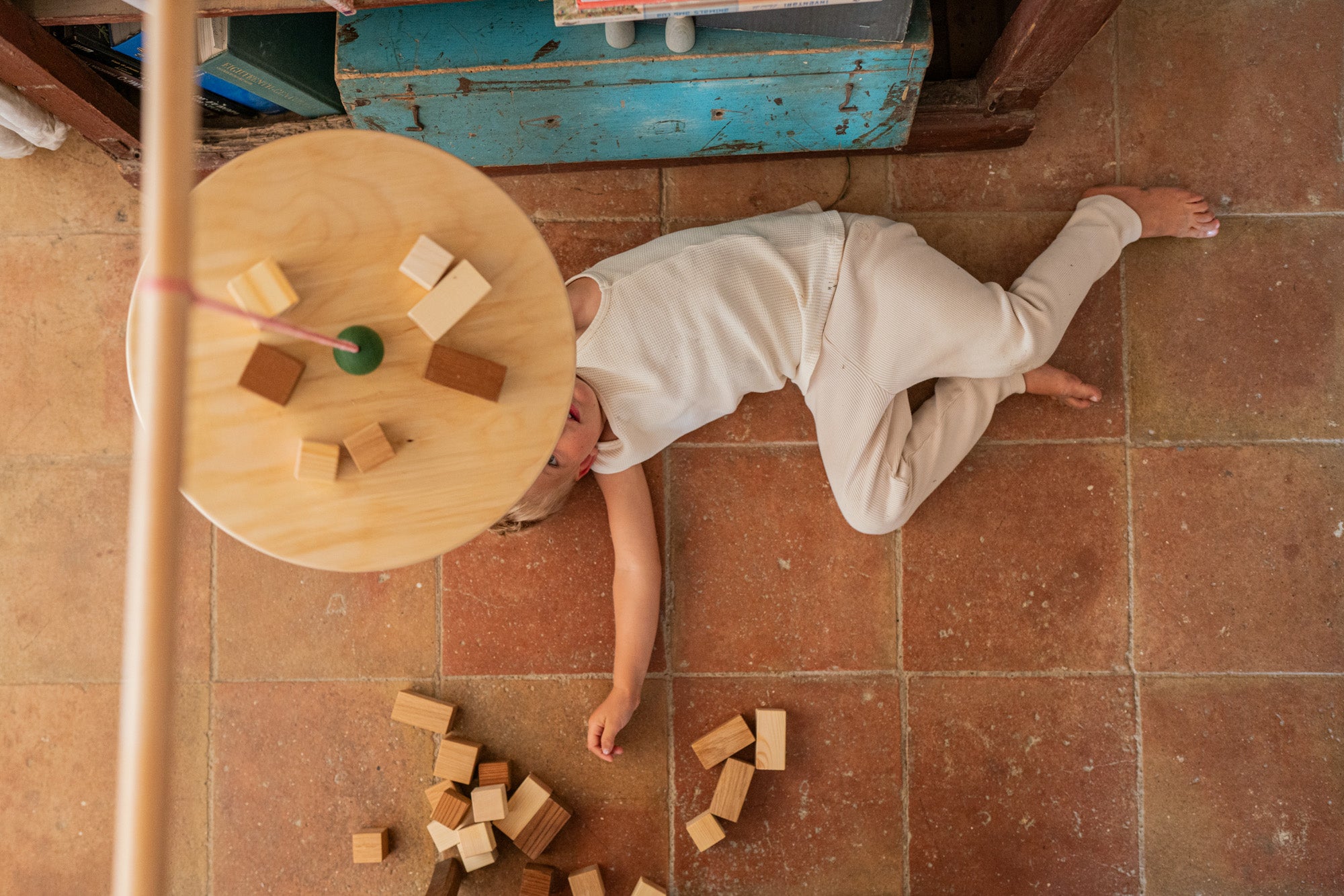 A child lying under the  Grapat wooden pendulum set with wooden blocks on the floor