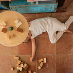 A child lying under the  Grapat wooden pendulum set with wooden blocks on the floor