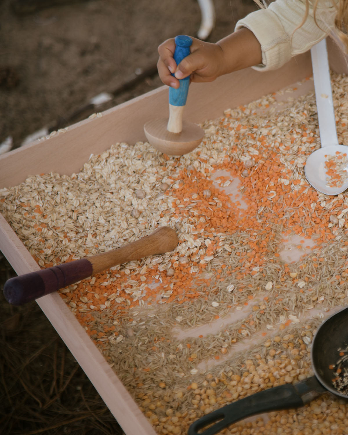 A child looking down at one of the Grapat Wooden Sensory Play Tools. The tool is being held by an adult who is different sized food items poked into the holes of the measuring tool