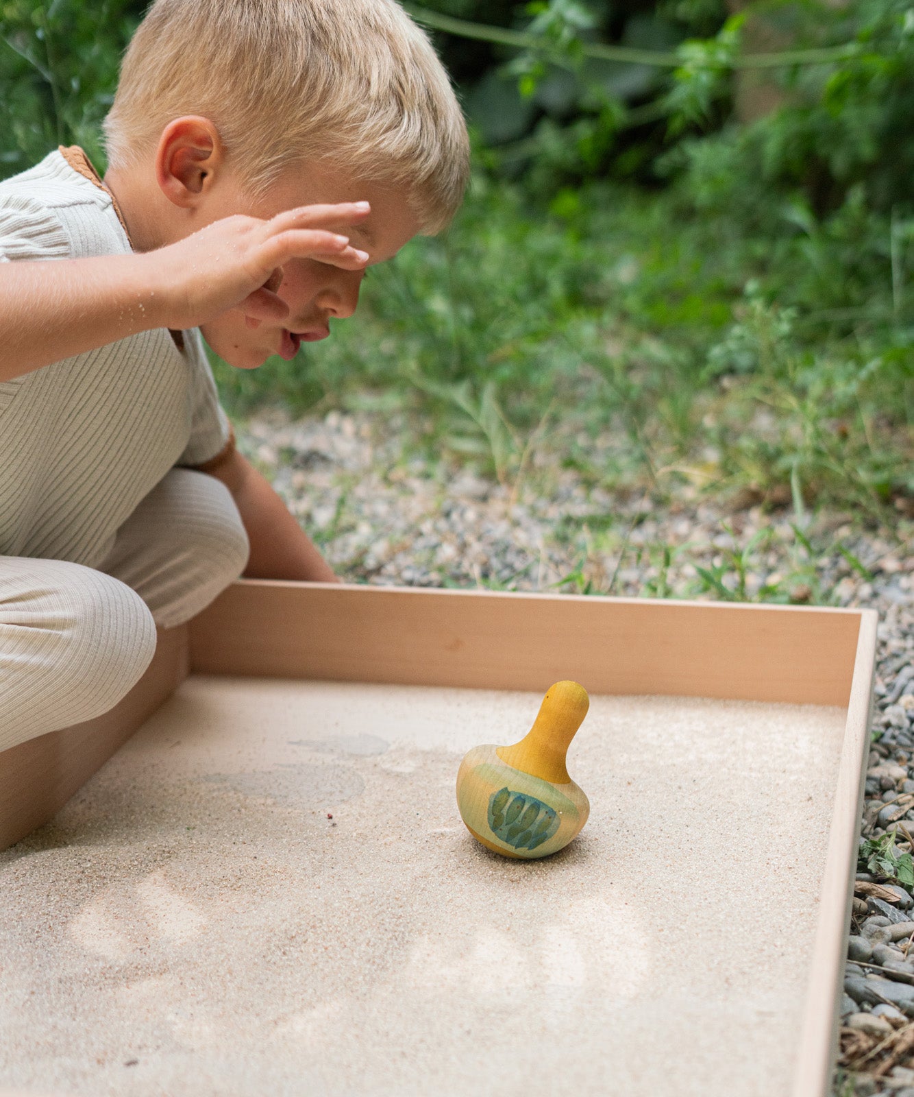 A child playing with the Grapat wooden yellow flowing bird outside in a sandpit 