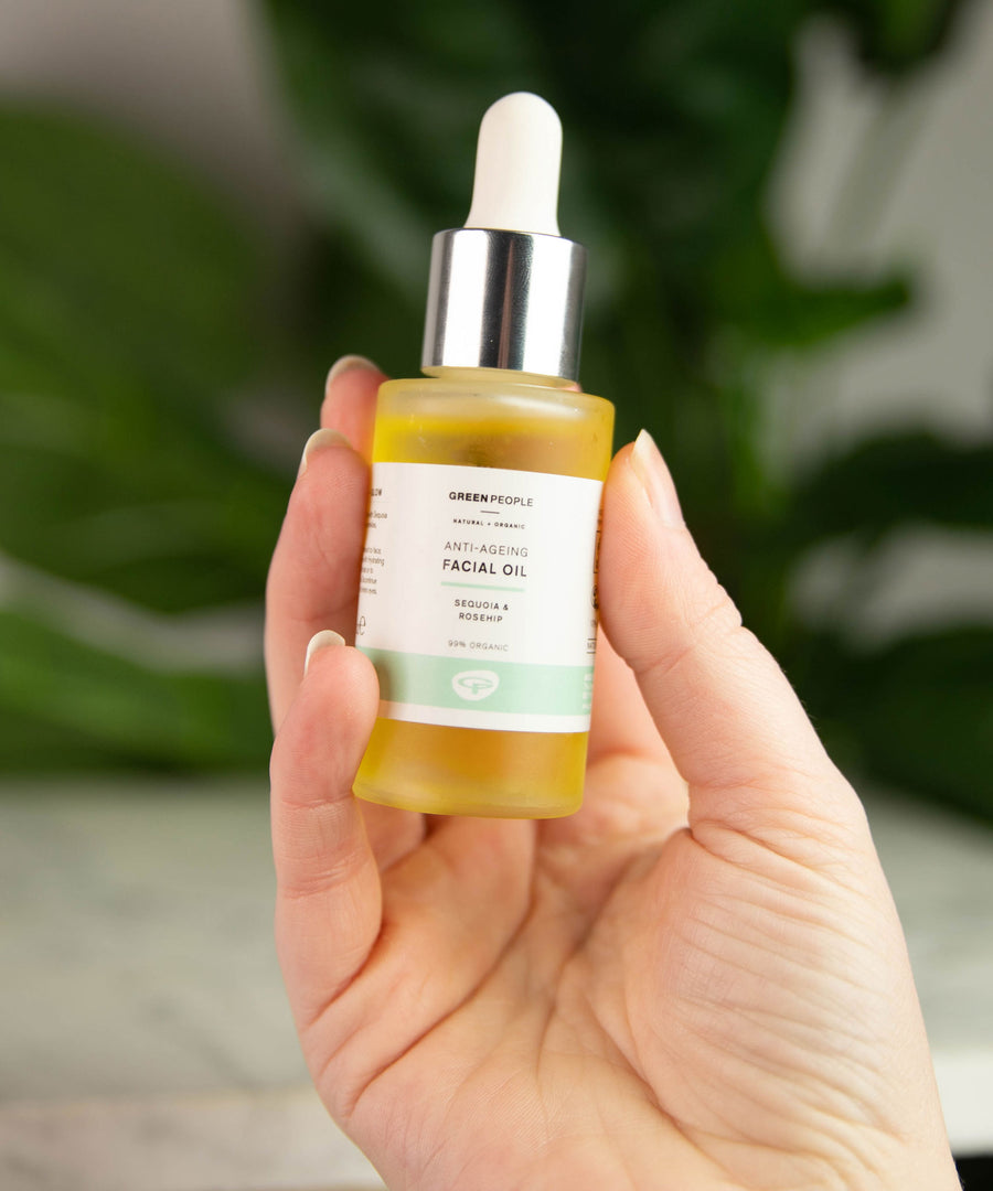 A bottle of Green People Anti-Ageing Facial Oil being held up in a persons hand. 