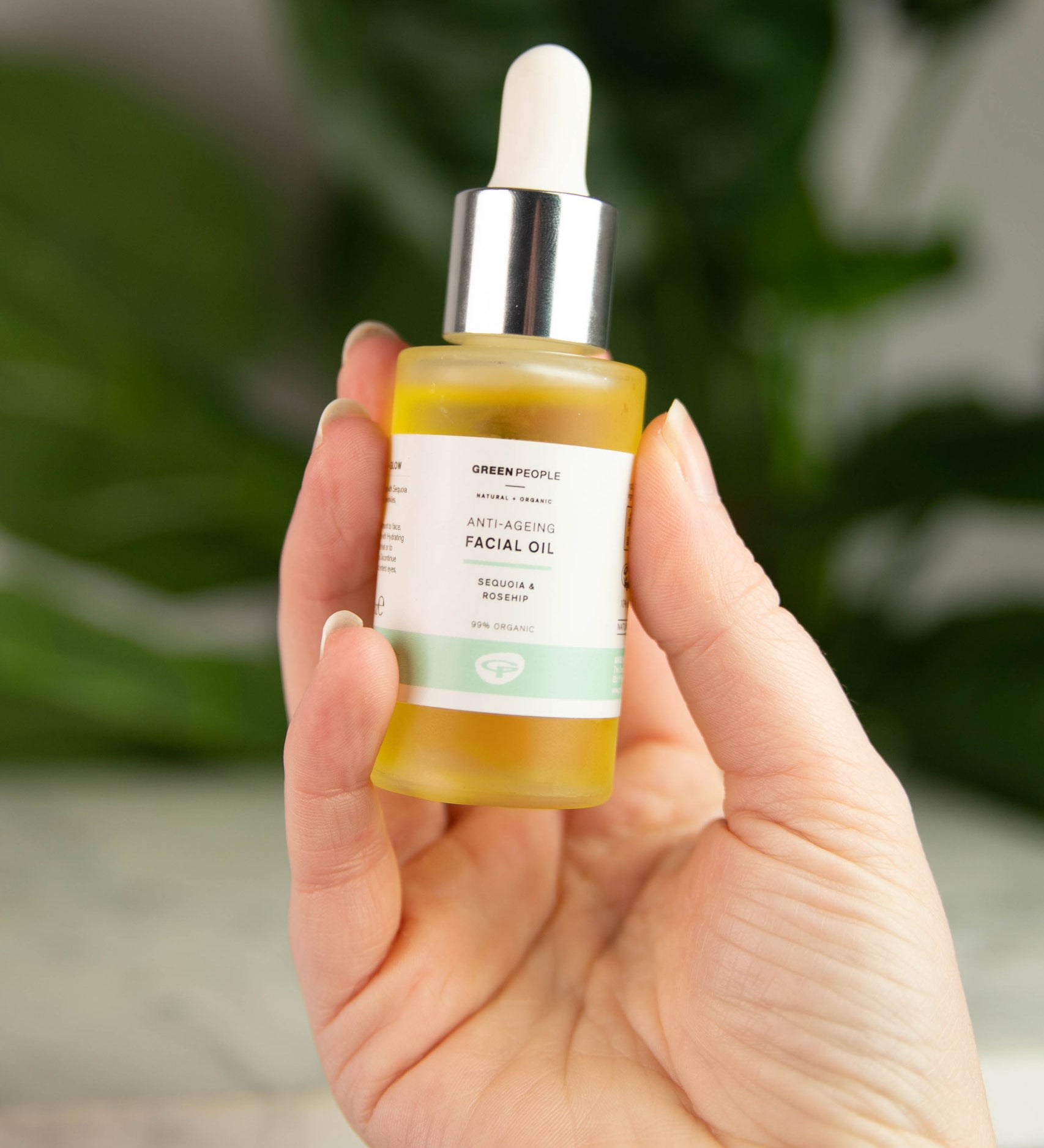 A bottle of Green People Anti-Ageing Facial Oil being held up in a persons hand. 