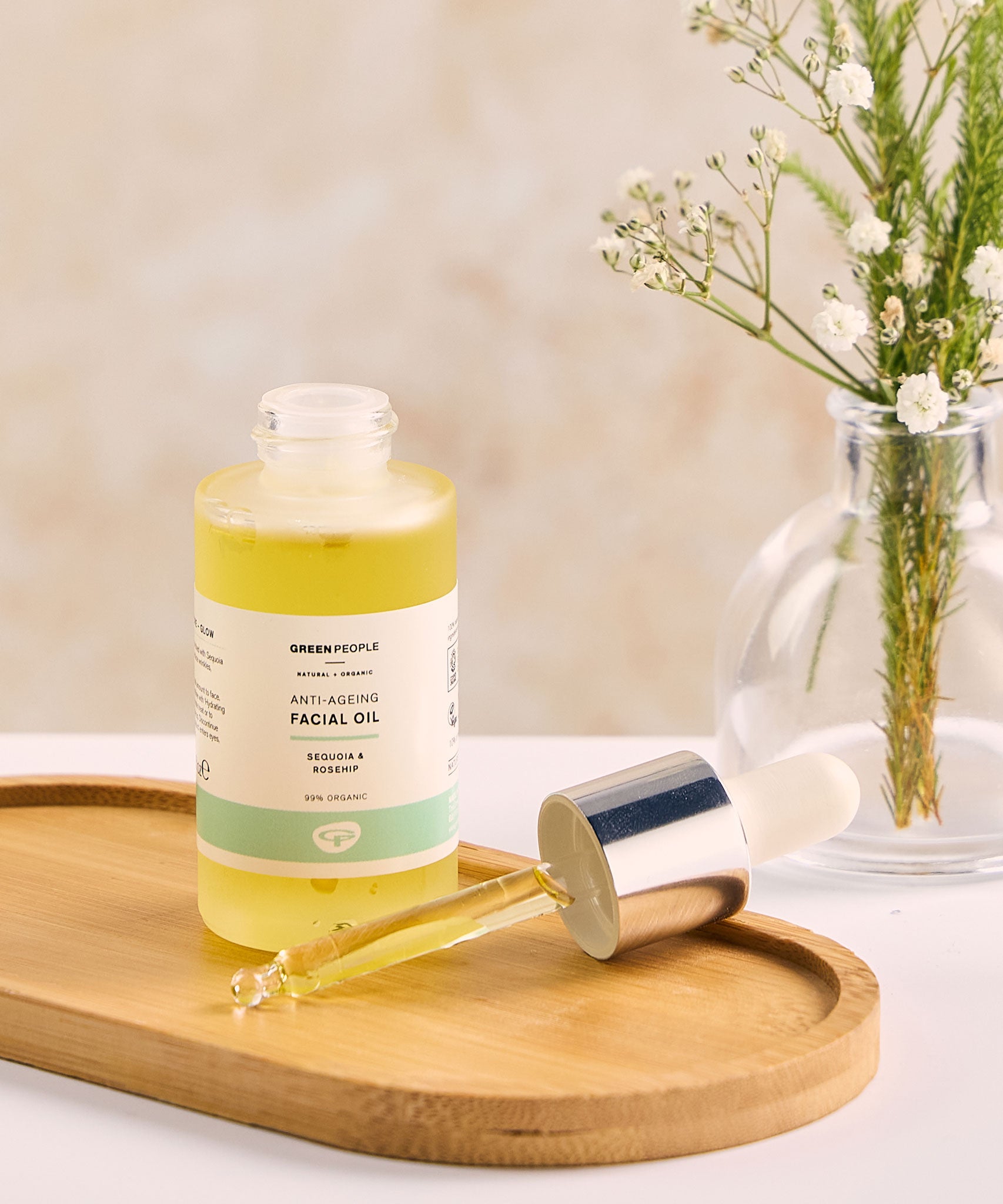 A bottle of Green People Anti-Ageing Facial Oil placed on an oval shaped bamboo dish. The pipette dispenser lid is resting besides the bottle on the dish 