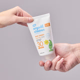 Two hand holding onto a tube of Green People Children SPF30 Sun Cream against a grey background. 