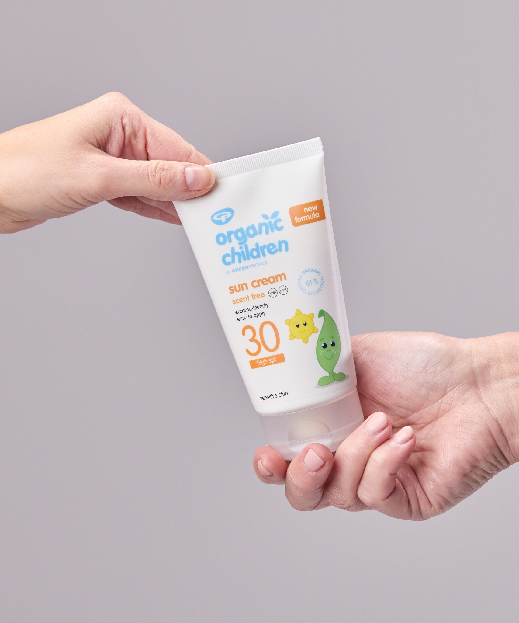 Two hand holding onto a tube of Green People Children SPF30 Sun Cream against a grey background. 