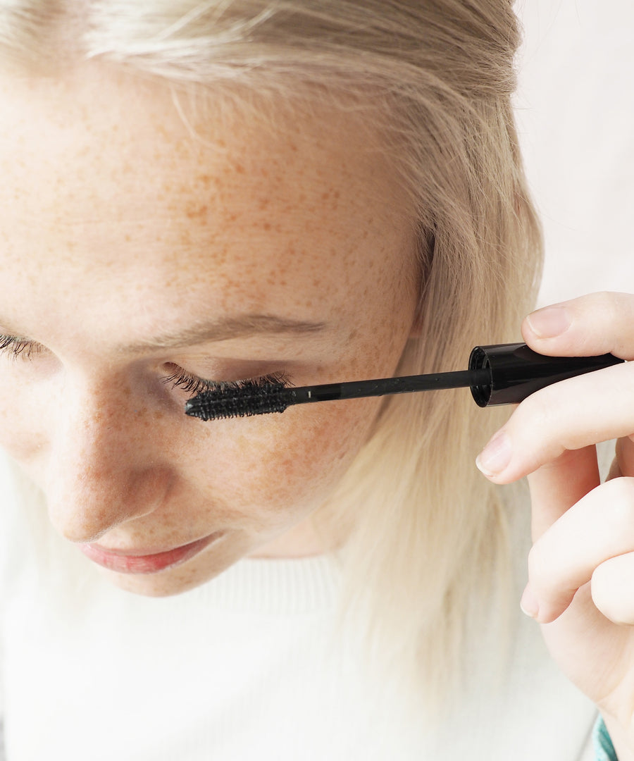 A person with blonde hair applying the Green People Volumising Black Mascara to their eyelashes.