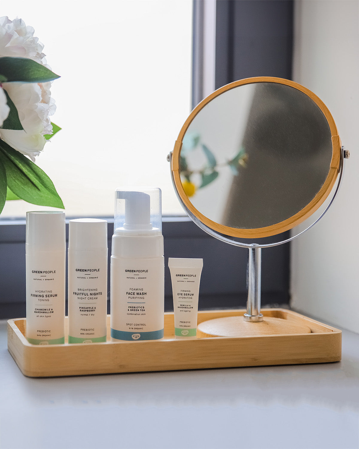 A collection of Green People facial care in a bathroom setting. The products are placed in a bamboo dish. 