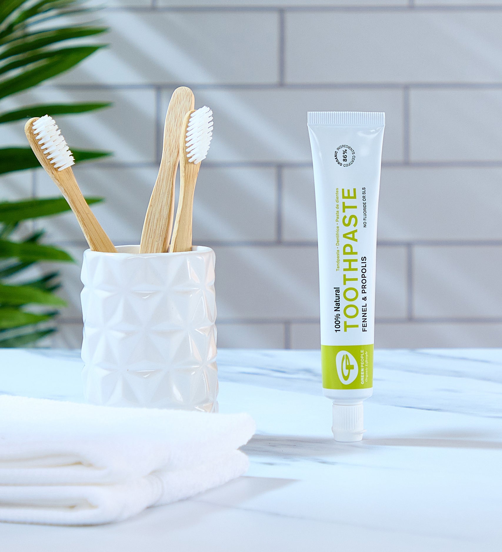 Green People Fennel & Propolis Natural Toothpaste on a marble surface in a bathroom next to a ceramic pot with bamboo toothbrushes.