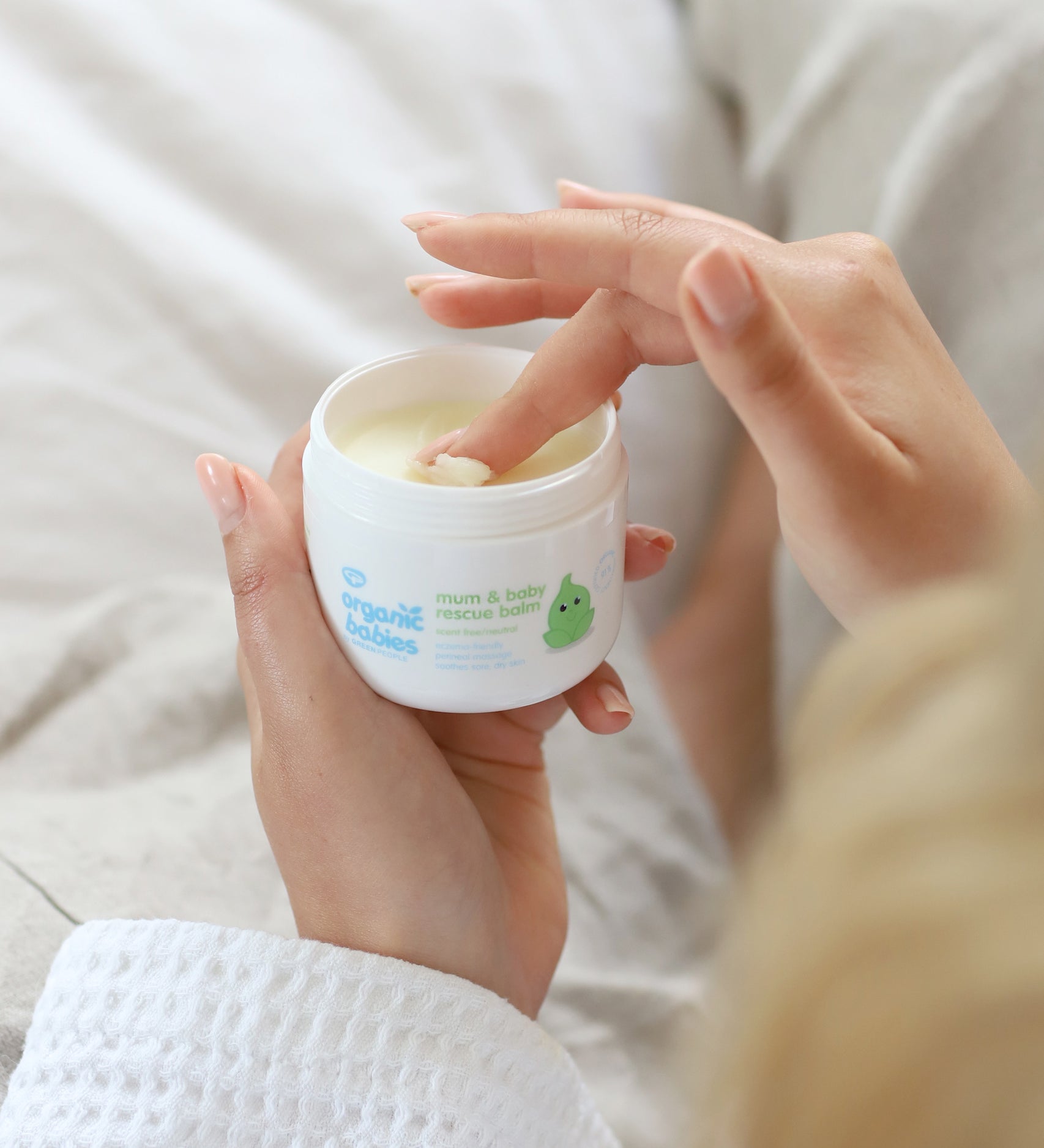 A close up of an adult's hand scooping some product out of the Organic Babies Mum & Baby Rescue Balm pot with their finger. 