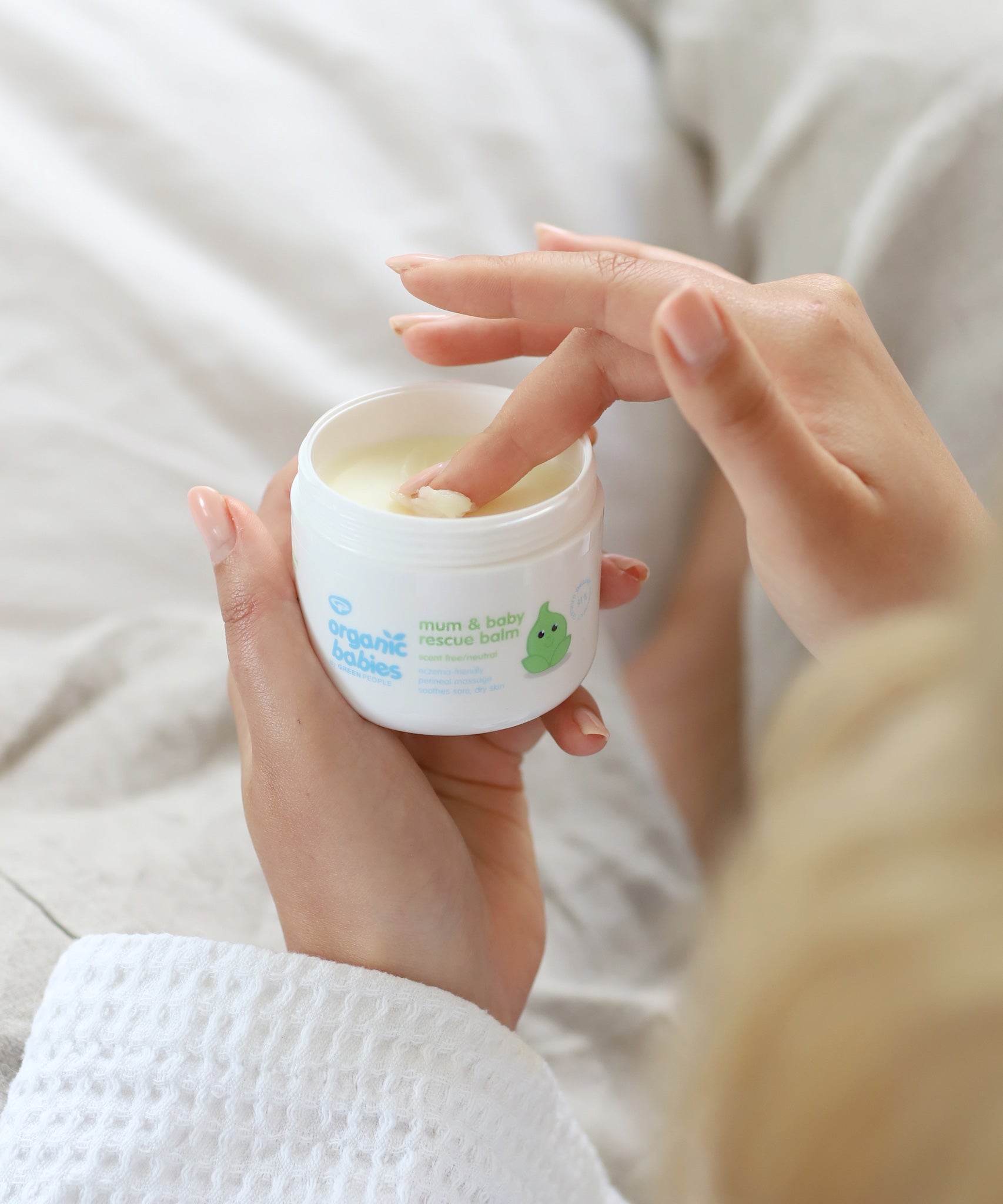 A close up of an adult's hand scooping some product out of the Organic Babies Mum & Baby Rescue Balm pot with their finger. 