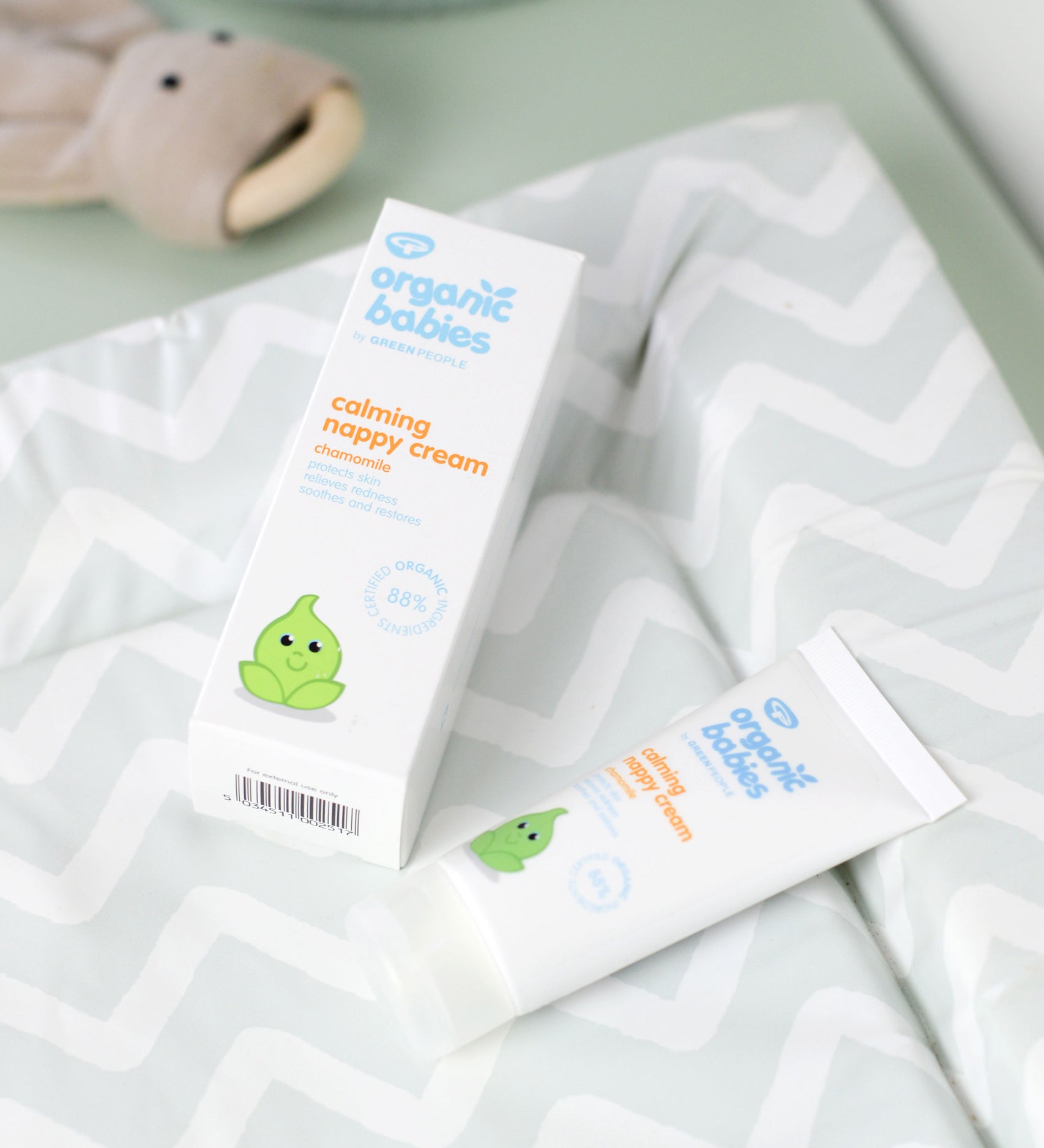 A tube of Organic Babies Nappy Cream Baby Balm placed on a changing mat next to the box.