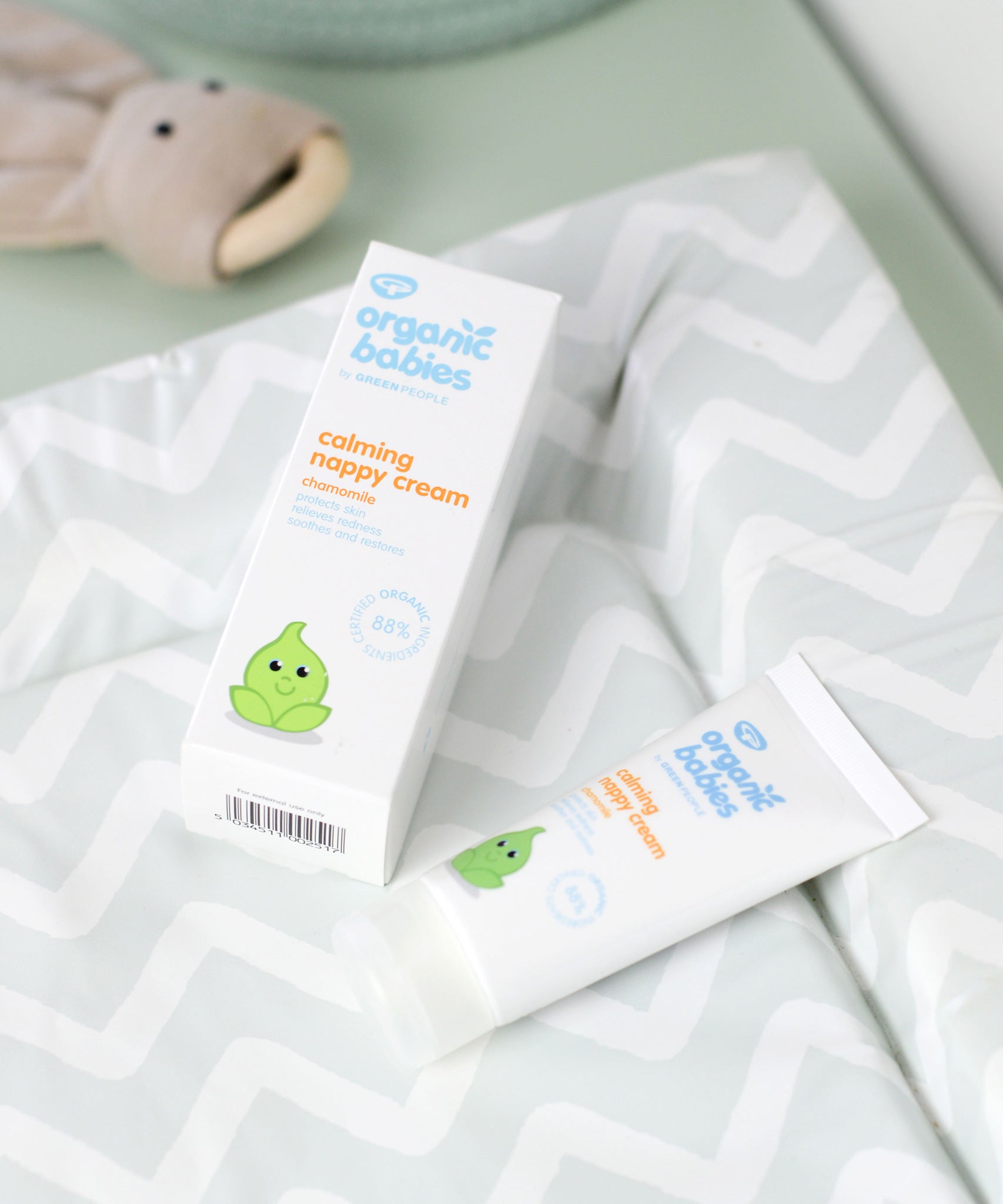 A tube of Organic Babies Nappy Cream Baby Balm placed on a changing mat next to the box.