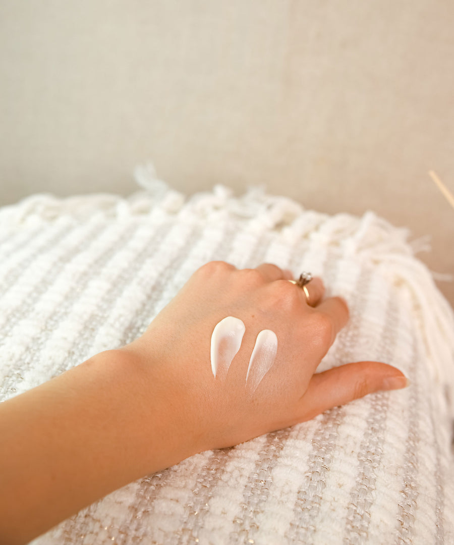 A swatch of the Green People Fruitful Nights Night Cream on a hand. The person is resting their hand on a striped blanket. 