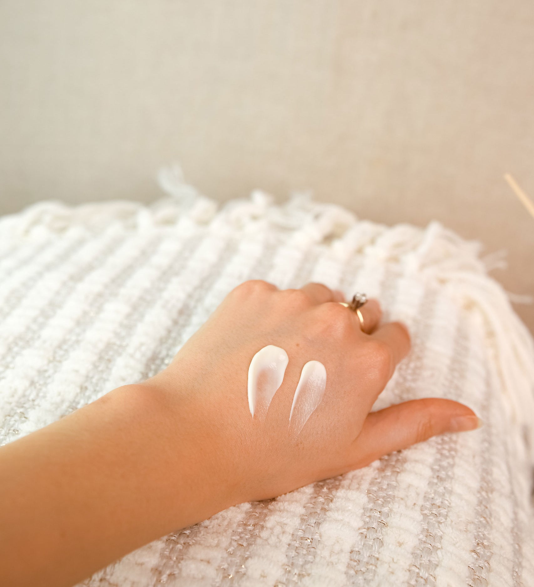 A swatch of the Green People Fruitful Nights Night Cream on a hand. The person is resting their hand on a striped blanket. 