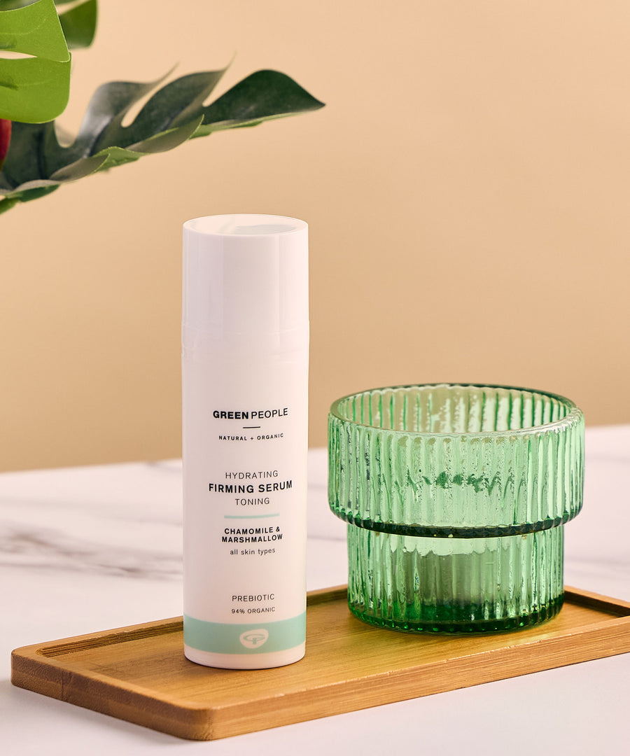 Green People Hydrating Firming Serum placed on a rectangular bamboo dish next to a green glass tealight holder. 