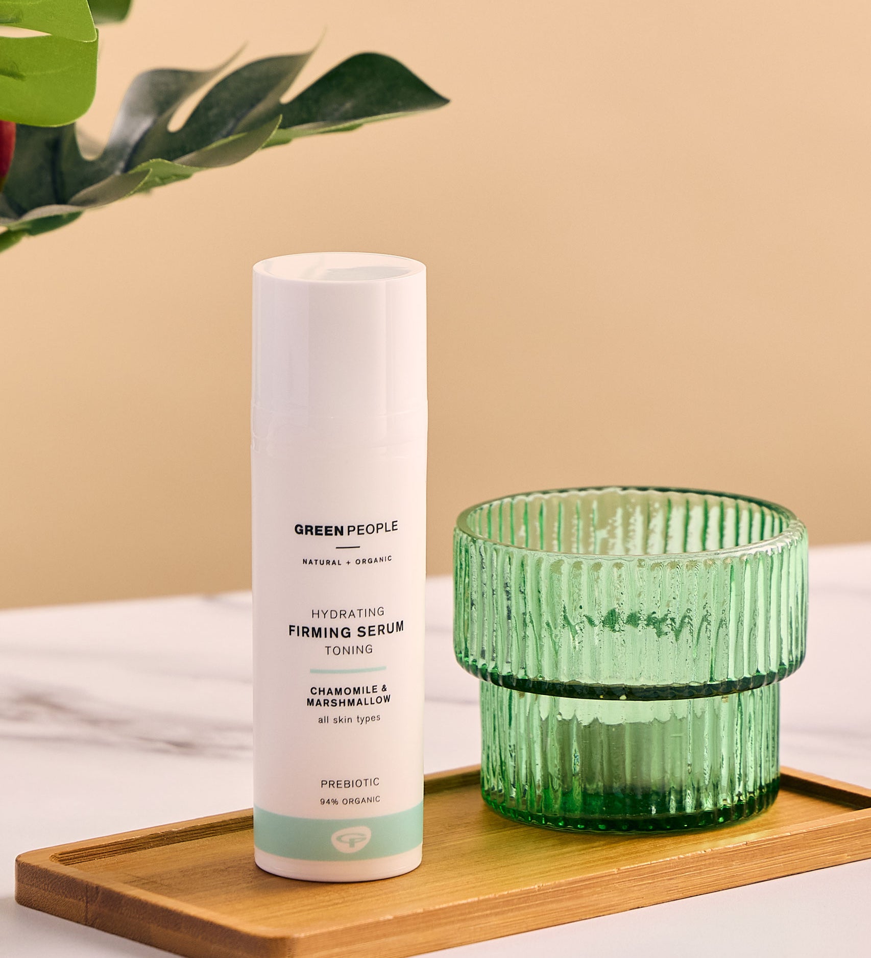 Green People Hydrating Firming Serum placed on a rectangular bamboo dish next to a green glass tealight holder. 