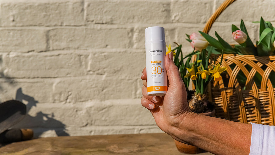 A person holding Green People SPF suncream with flowers in the background.