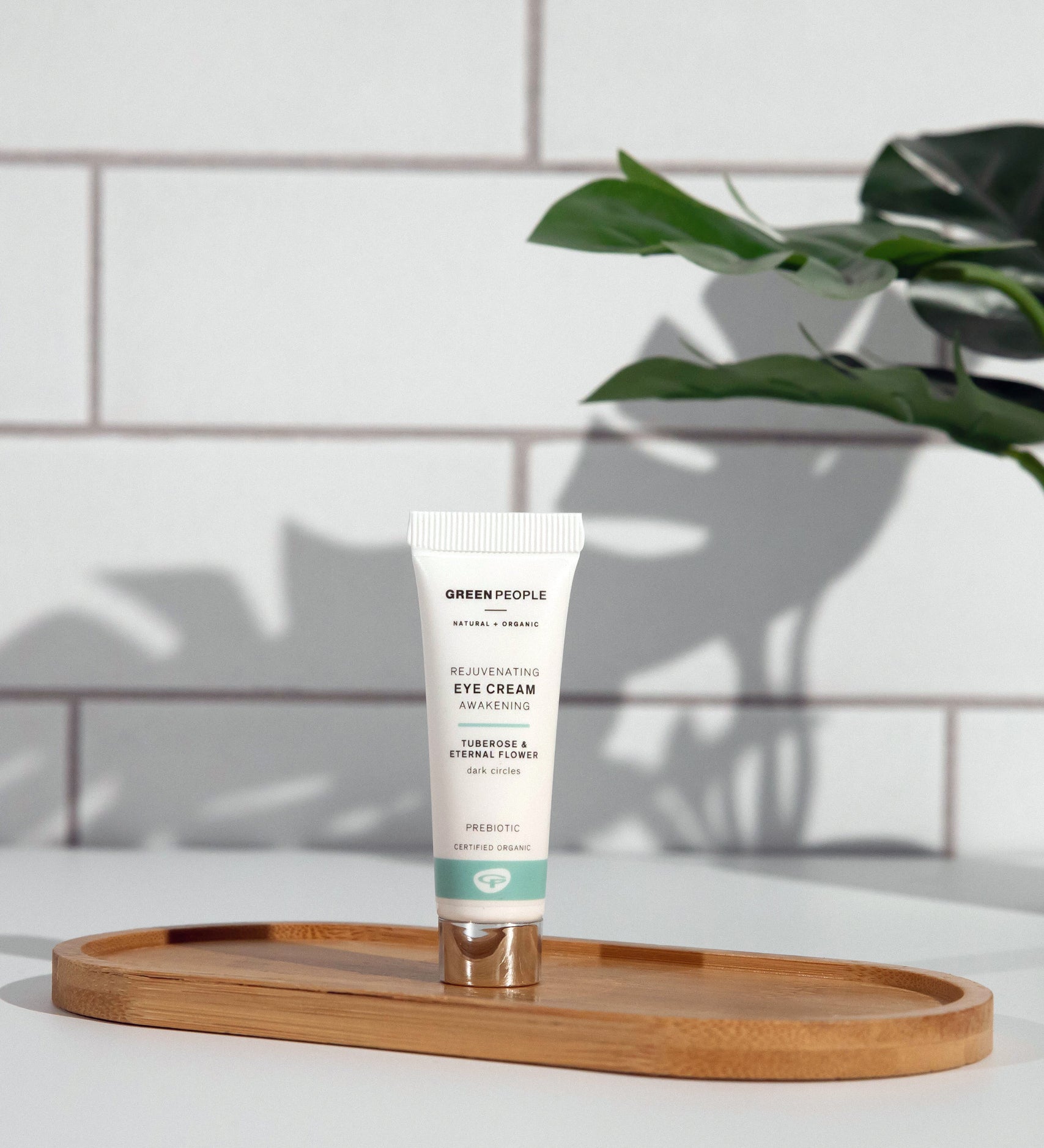 A tube of Green People Rejuvenating Eye Cream placed on an oval shaped bamboo tray in a bathroom. 