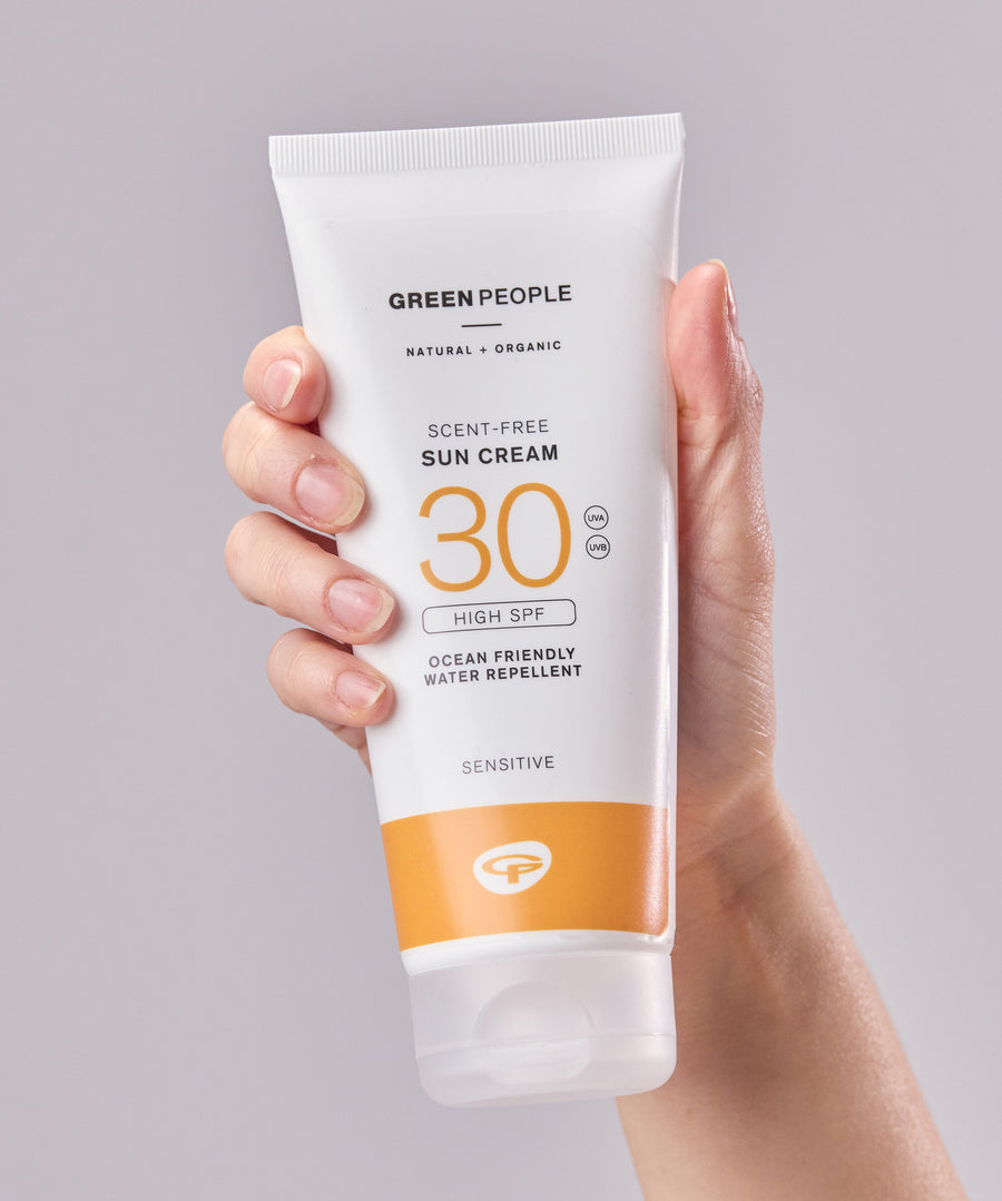 A tube of Green People Sun Cream SPF30 in an adult's hand. 