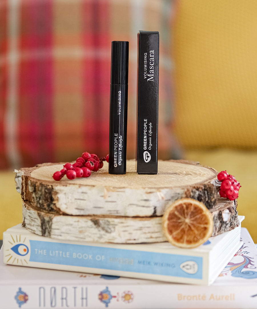 A pack of Green People Volumising Mascara on a log slice that has been placed on a pile of books. 