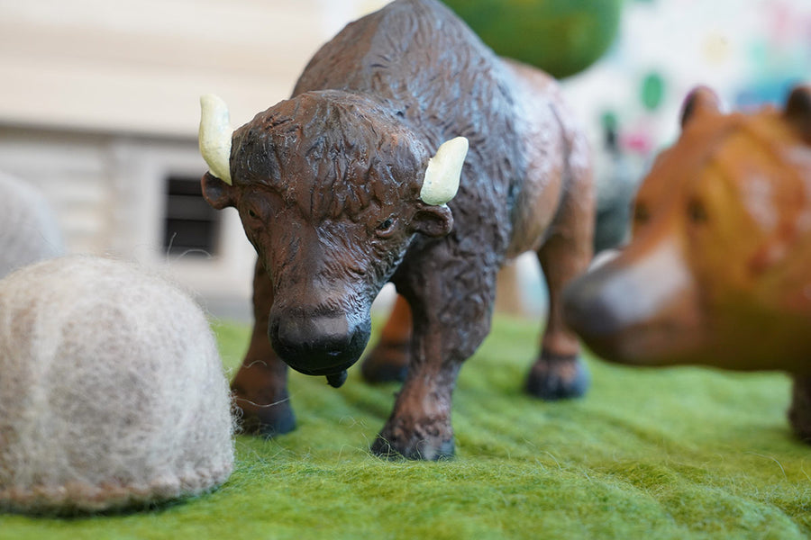 Green rubber toys bison figure on some green felt behind a papoose rock toy