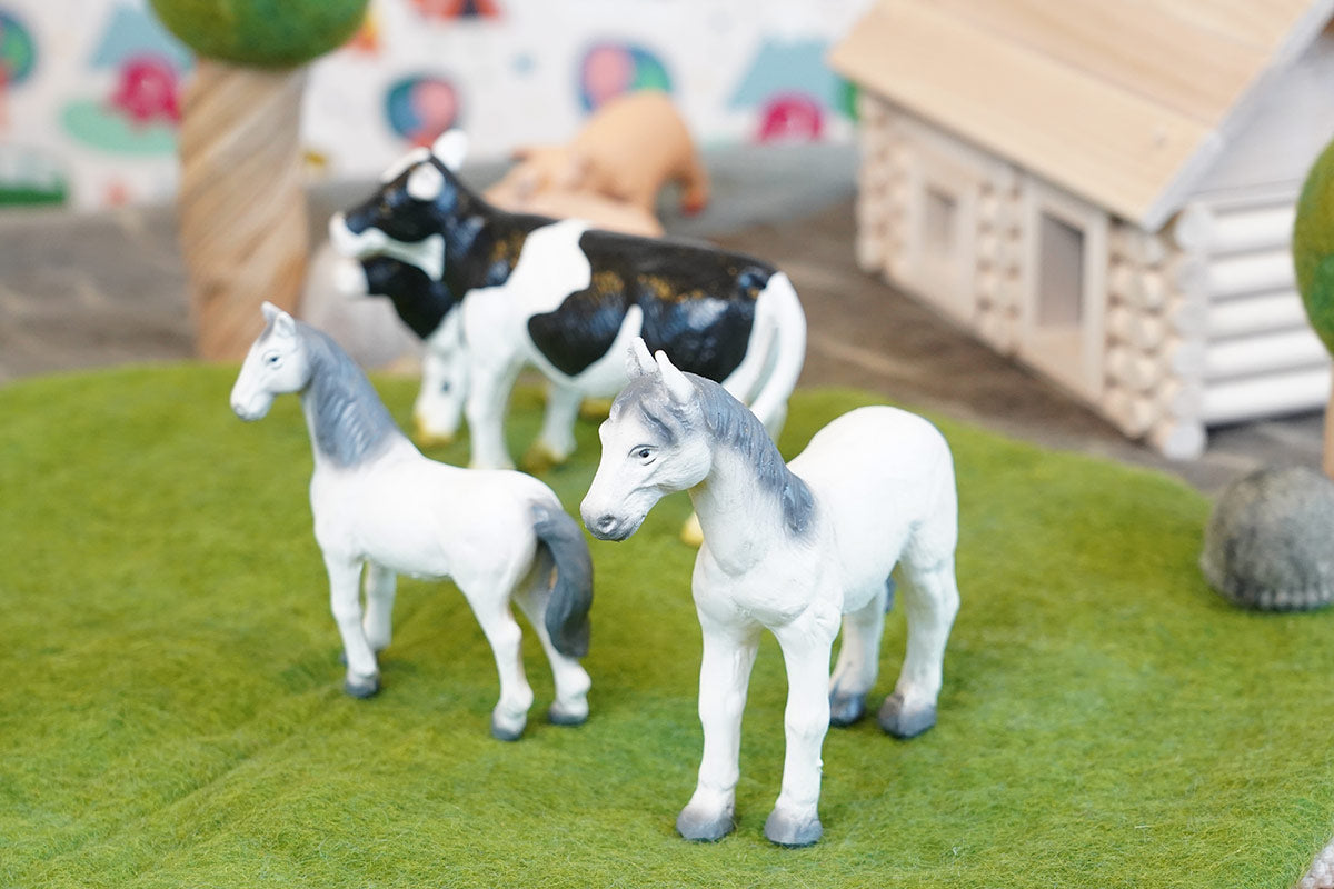 Green rubber toys horses stood on some green felt in front of some green rubber toys cows