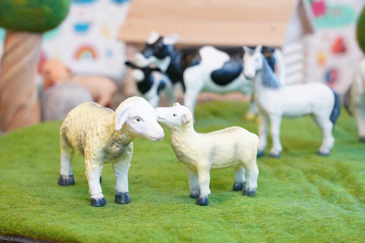 Green rubber toys sustainable sheep figures stood on some green felt in front of a horse and cow toy