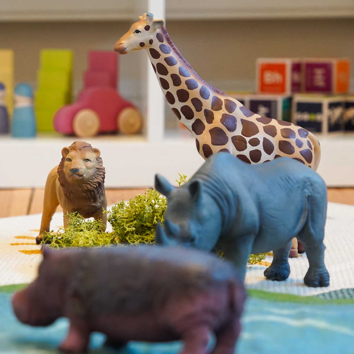 play scene with Green Rubber Toys Jungle Animals Set with the lion and giraffe in focus in the back and rhino and hippo out of focus in the foreground