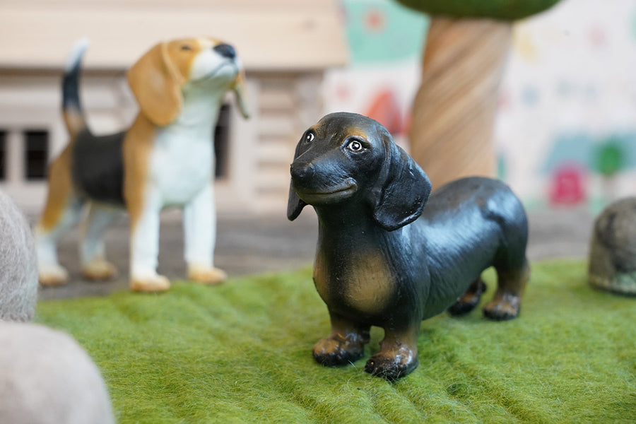 Green rubber toys dachshund and beagle stood on some green felt in front of a wooden toy tree