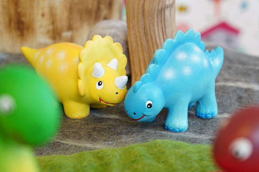 Close up of the green rubber toys mini dinosaurs stood on some grey felt in front of a papoose tree toy