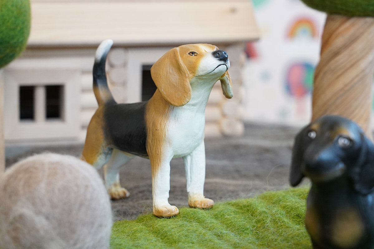 Green rubber toys eco-friendly beagle figure stood on some green felt in front of a small wooden house toy