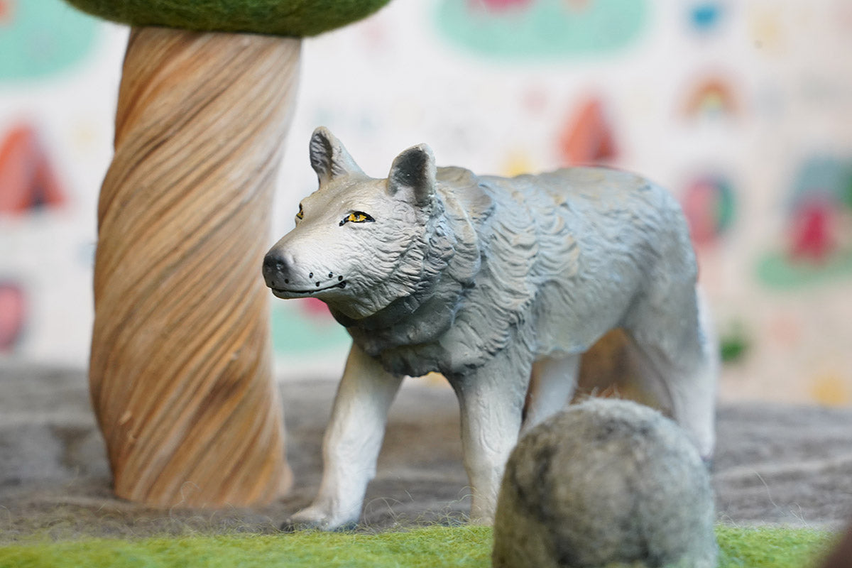 Close up of a green rubber toys sustainable wolf on some green felt in front of a papoose wooden tree toy